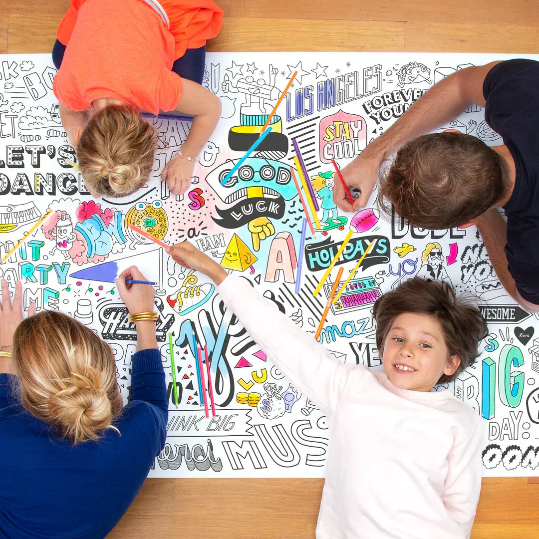 Enfants et parents en train de colorier un poster géant OMY sur le sol pendant une fête d’anniversaire à la maison
