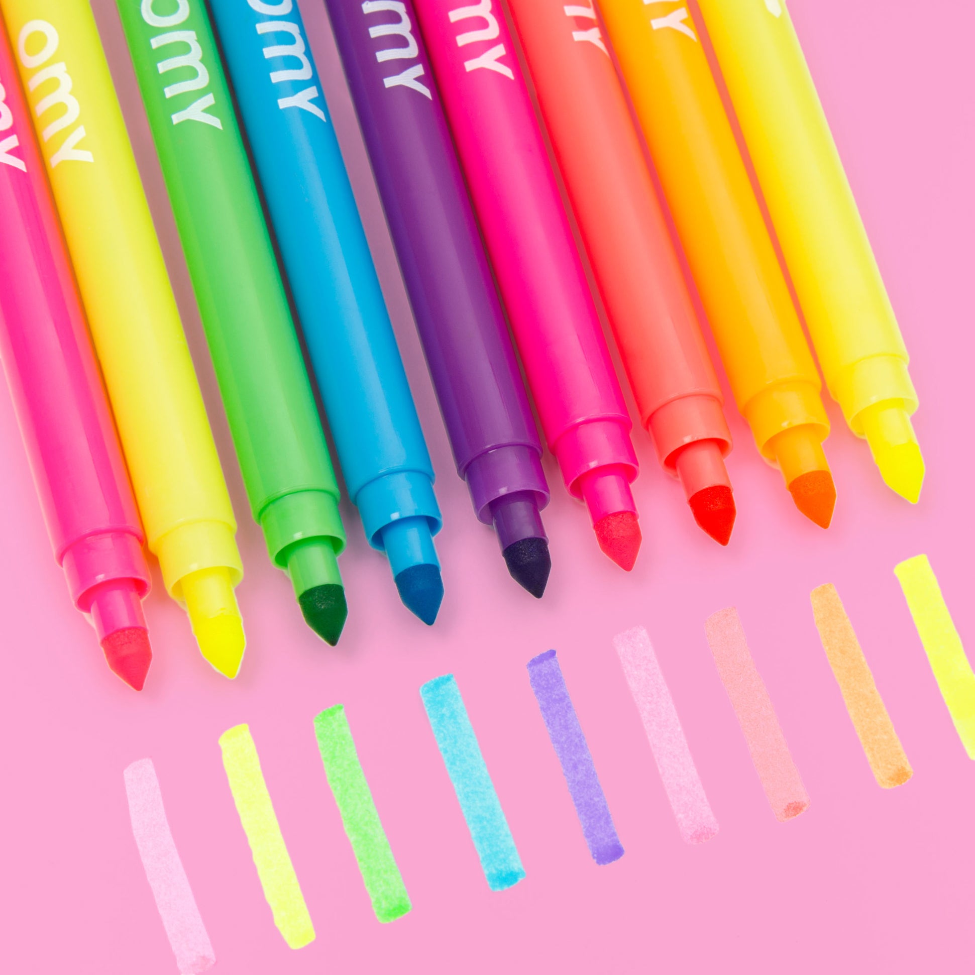 Crayons feutres fluo OMY posés sur table rose – Kit de coloriage DIY