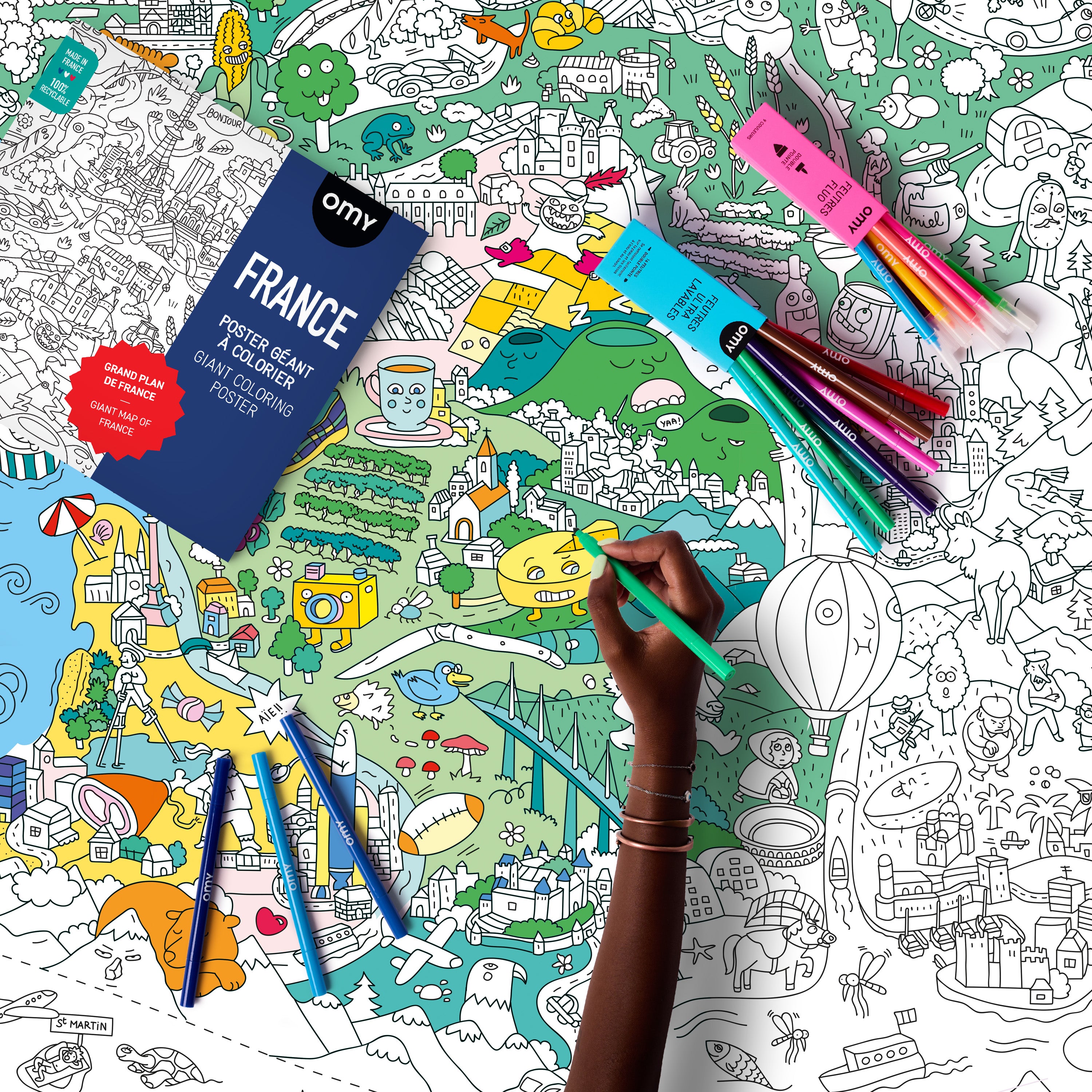 Enfant coloriant le poster géant OMY « France » avec des feutres colorés, mettant en valeur les régions françaises et leurs symboles culturels dans une scène créative et éducative.