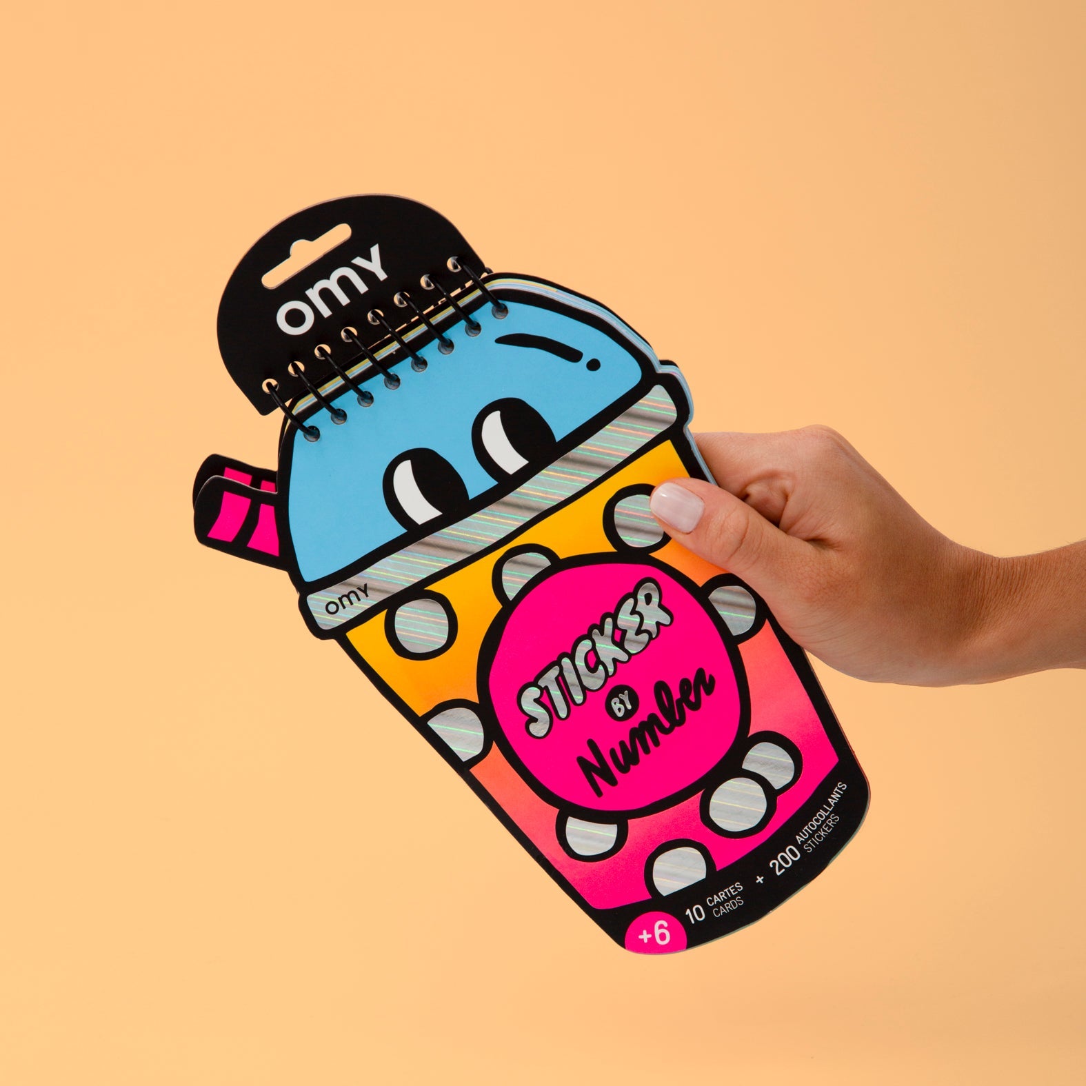 Main tenant le carnet Sticker by Number Bubble Tea OMY en forme de gobelet : 10 cartes et 200 autocollants, dès 6 ans