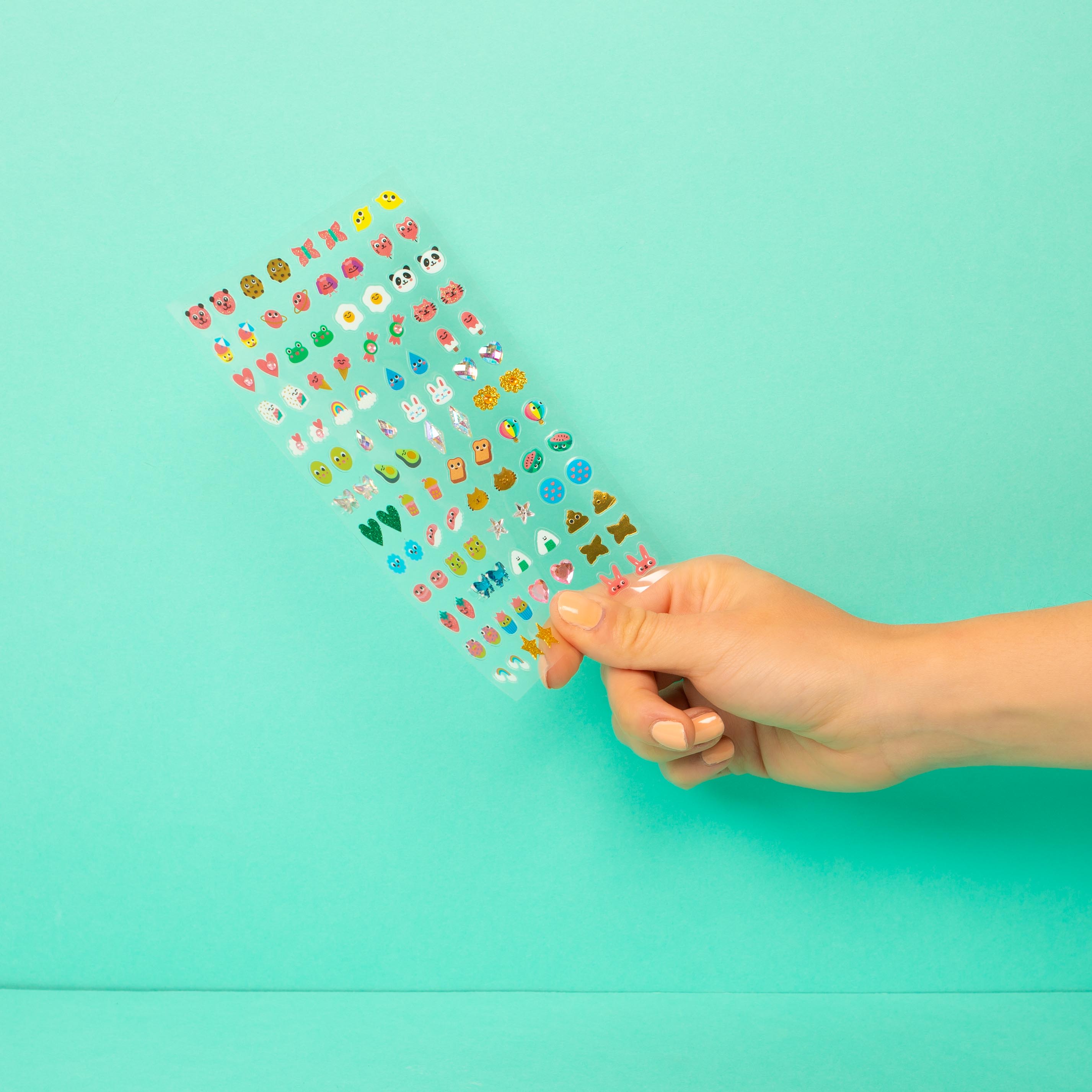 Main présente planche bijoux autocollants OMY Kawaii pour oreilles enfant.