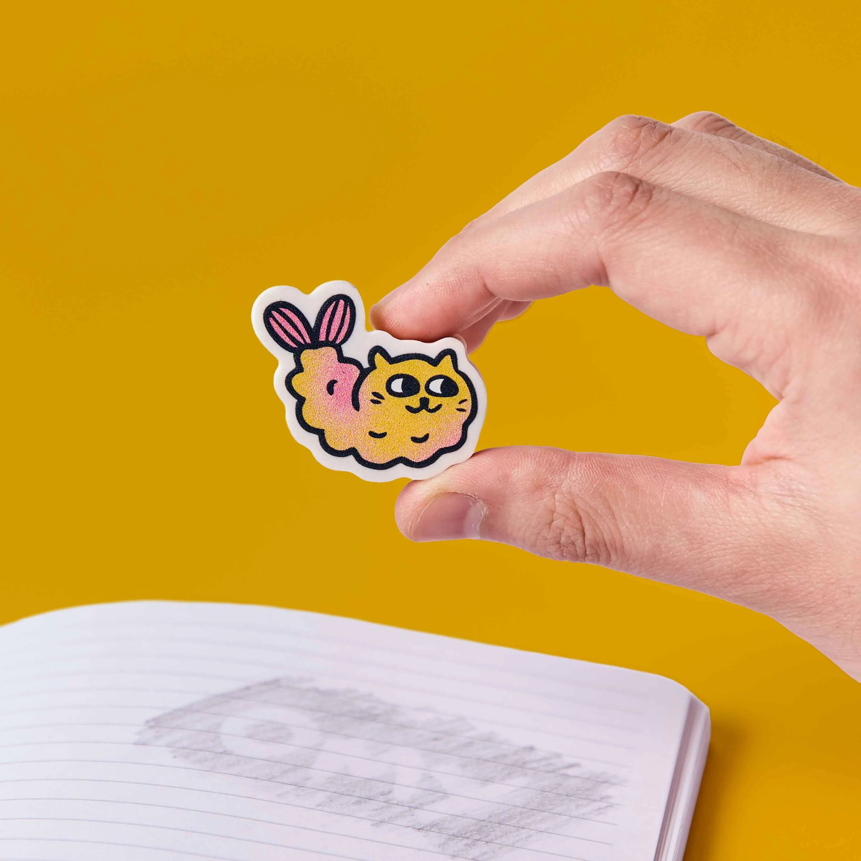 gomme chat kawaii Mewchi OMY tenue en main au dessus cahier ecole