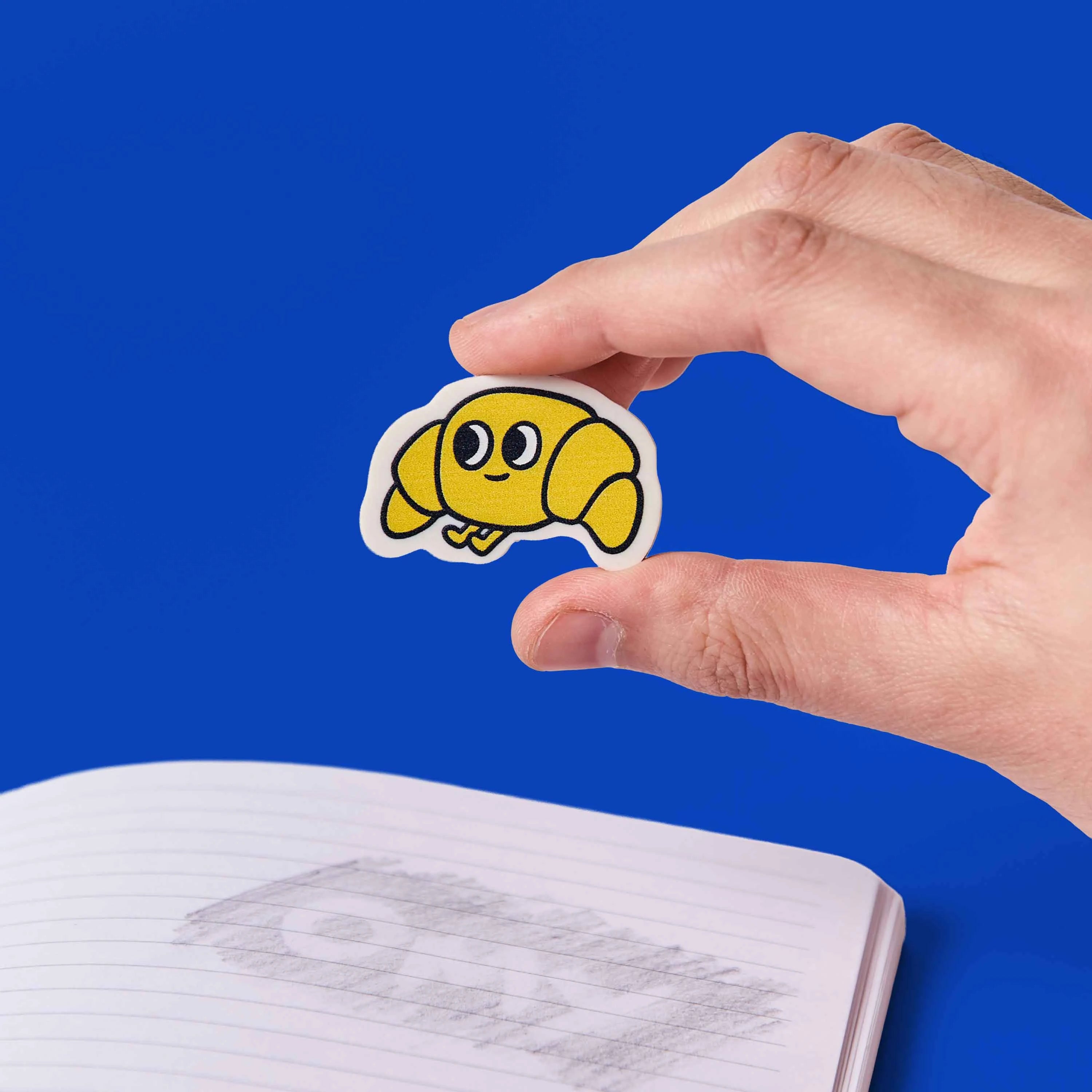 gomme croissant kawaii Leon OMY tenue en main au dessus carnet ecole