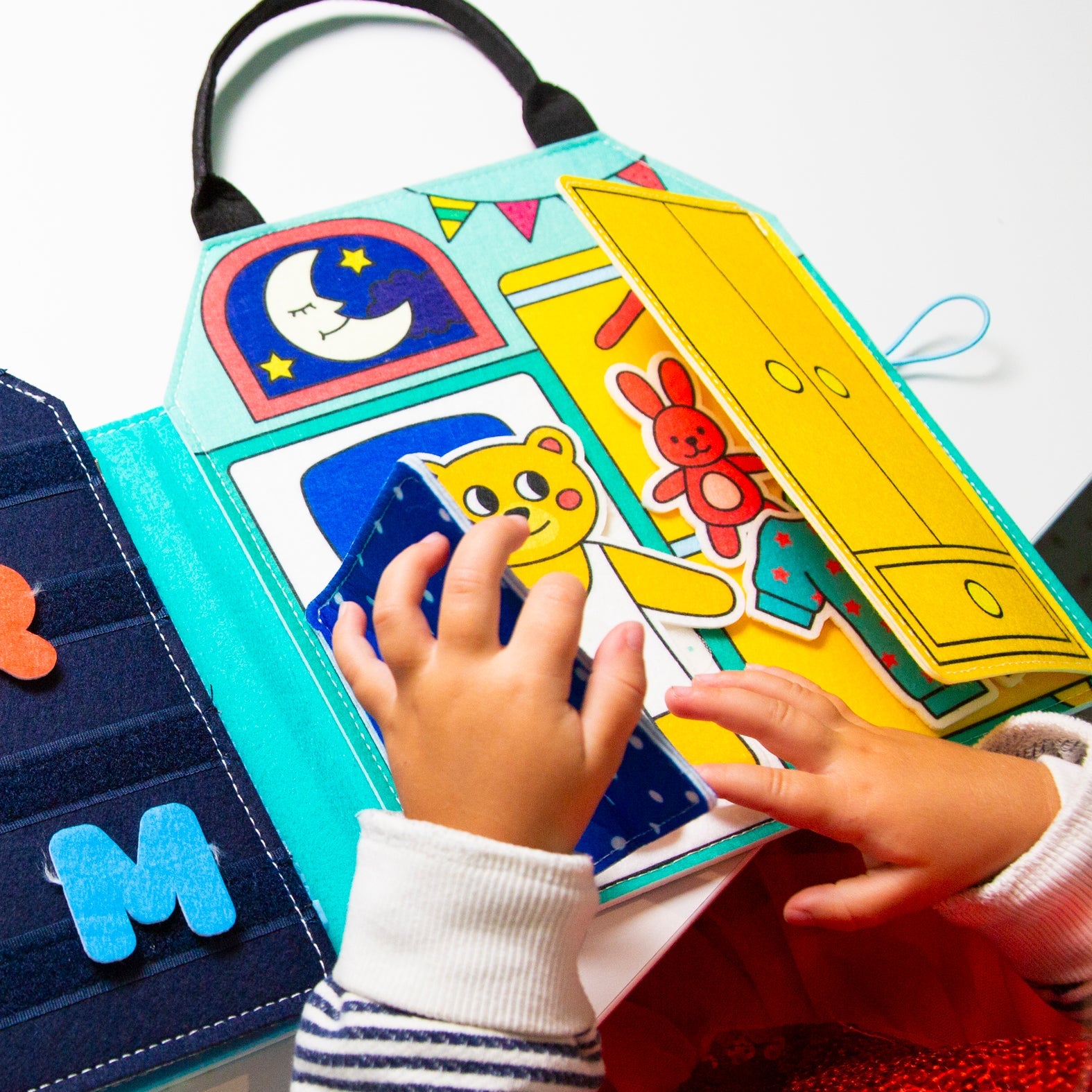 Child handling the OMY Little My Day felt activity book: teddy bear under the blanket, wardrobe to open, velcro letters.