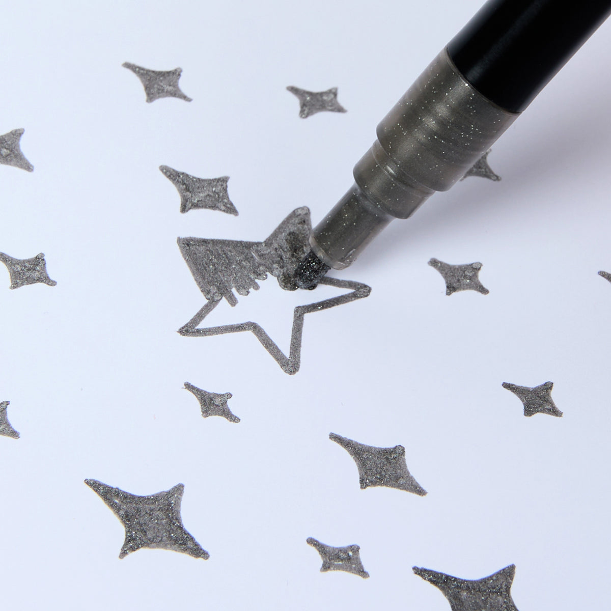 Feutre pailleté argent Glitter Club OMY en train de colorier une étoile sur papier.