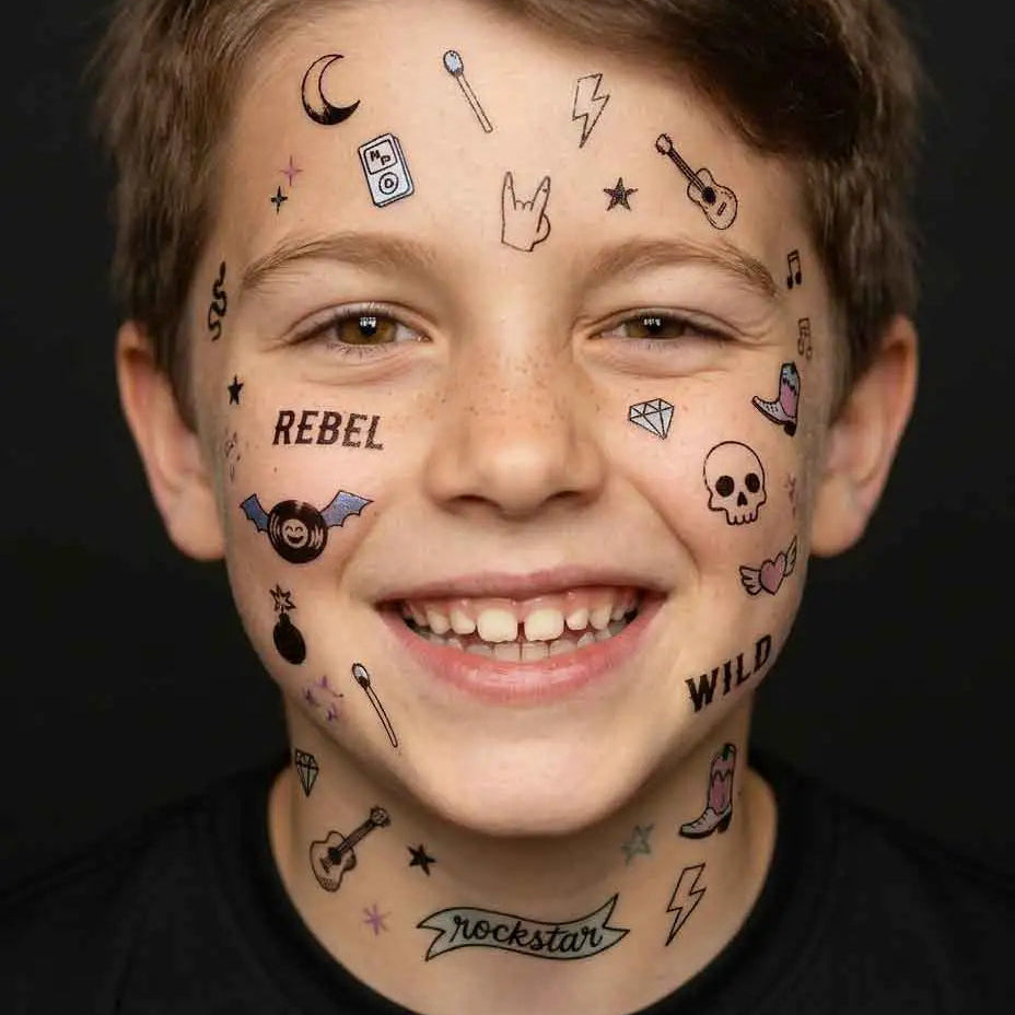Garçon souriant avec des tatouages temporaires OMY au style rock sur le visage (crâne, éclairs, guitare, lune, inscription REBEL et WILD), collection Flash Tattoos Wild Rebel – modèle Malone