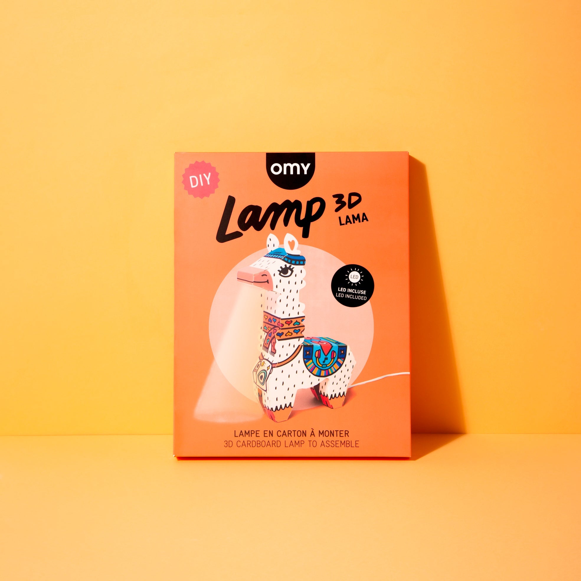 DIY-Box Lamp 3D Lama OMY: Lama-Lampe aus Karton zum Zusammenbauen, LED inklusive, auf orangefarbenem Hintergrund.