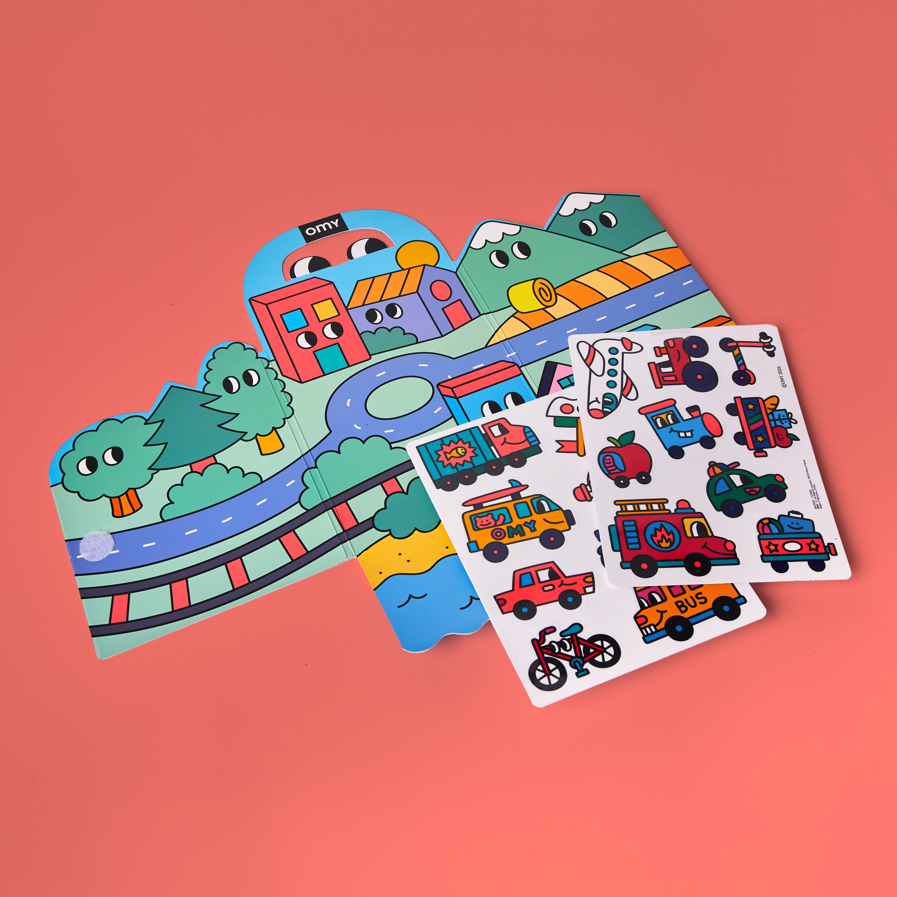 Kit d'autocollants Montessori - Vroom Vroom par OMY montrant le décor déplié avec routes et arbres et une planche de stickers véhicules sur fond rose – activité créative sans écran pour enfants