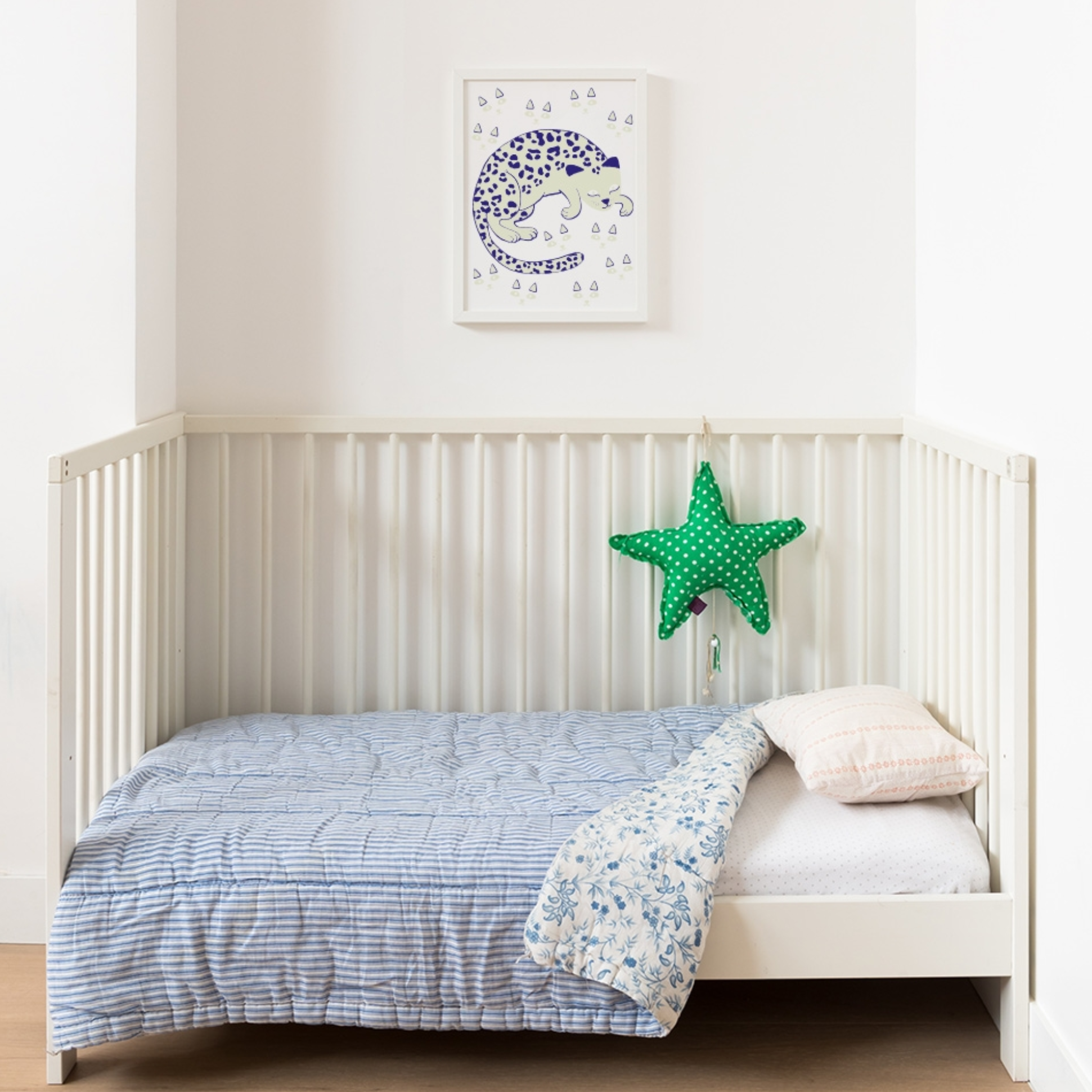 Kinderzimmer: gerahmtes blaues OMY Schneeleoparden-Poster über einem weißen Gitterbett mit Sternkissen