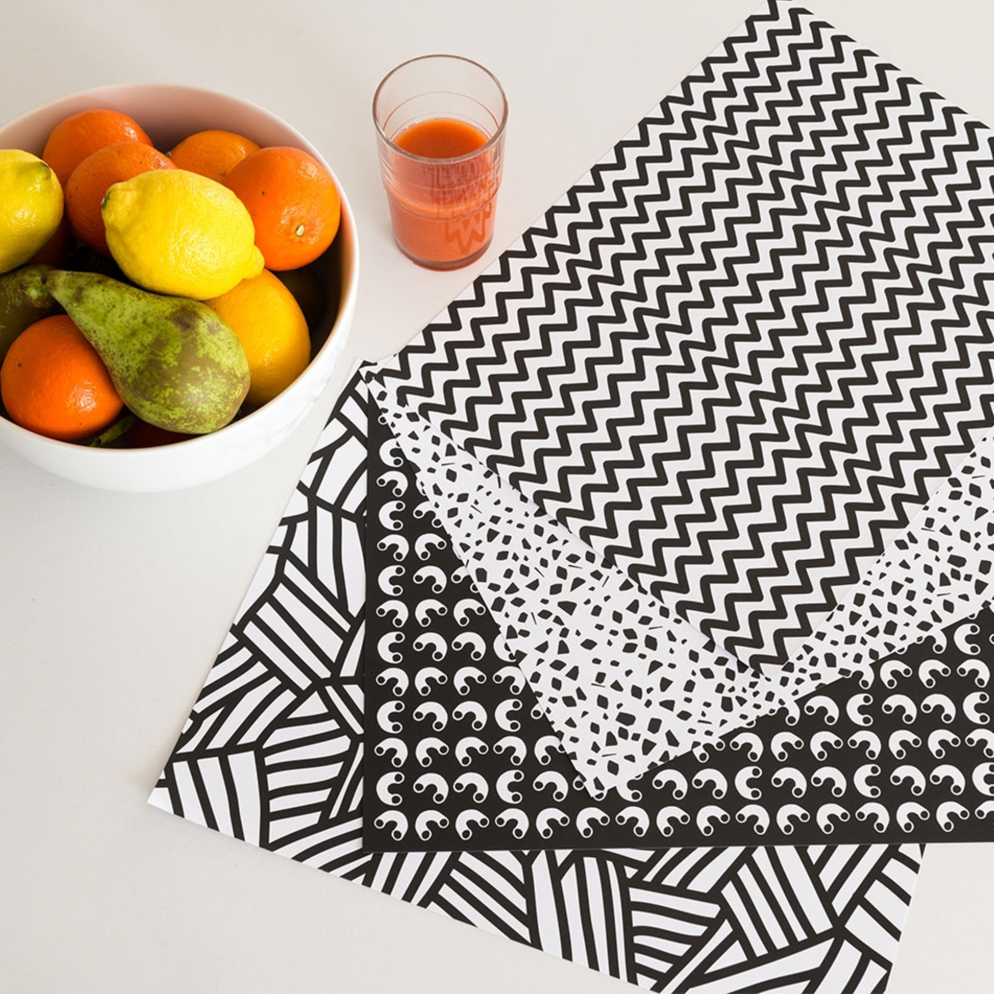 OMY Graphic.01 Papier-Tischsets mit 4 Mustern in Schwarzweiß auf einem Tisch, mit einer Obstschale und einem Saft