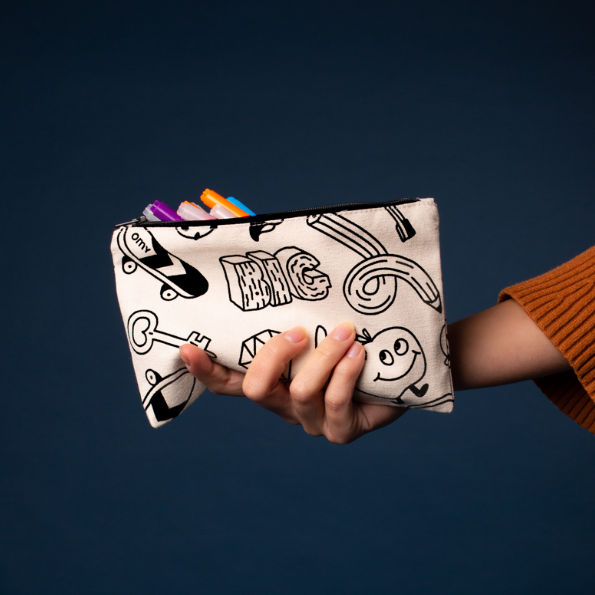 Hand hält das OMY Malmäppchen aus Rohleinen mit schwarz-weißen Motiven, Filzstifte ragen heraus, auf nachtblauem Hintergrund