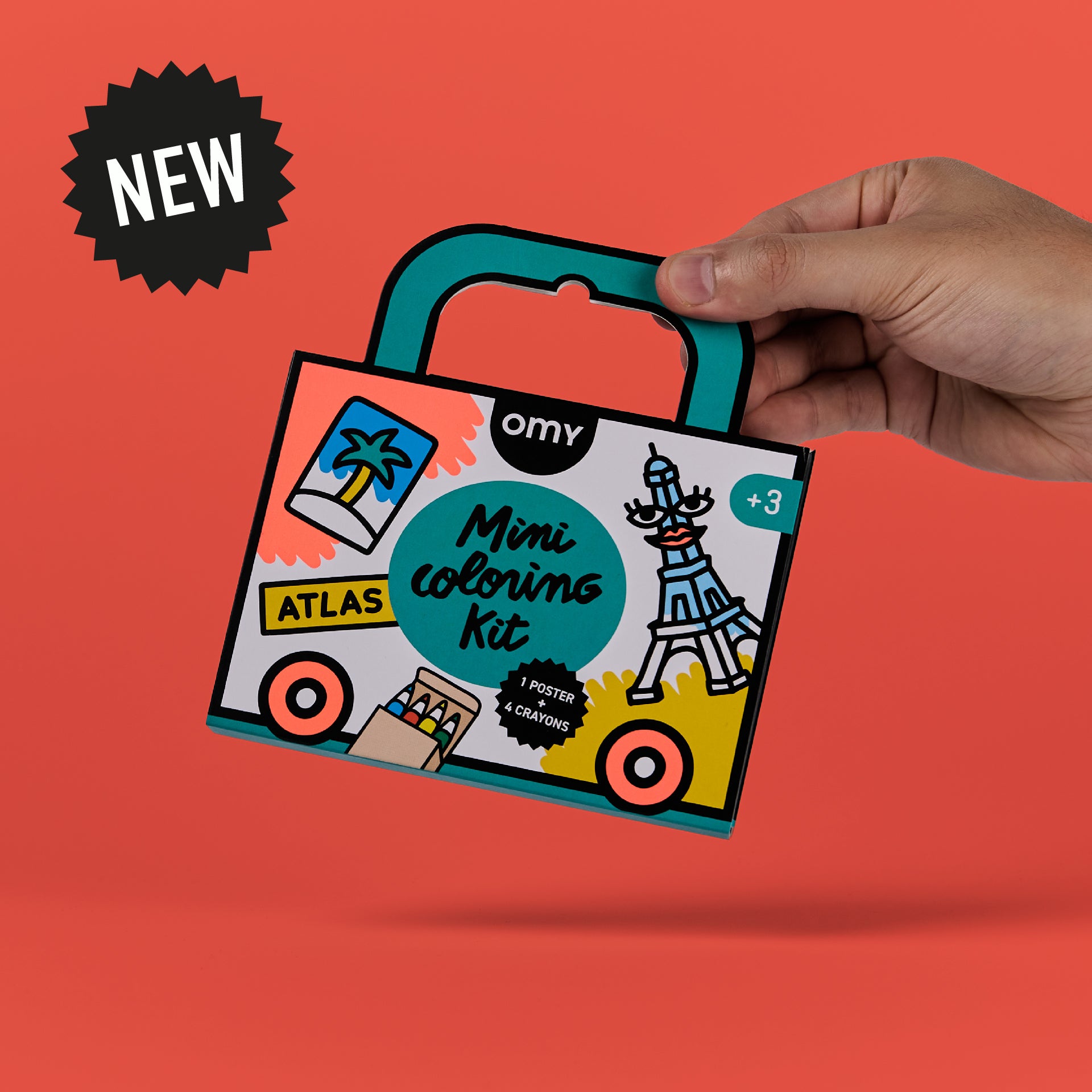 Main tenant le Mini Coloring Kit Atlas d’OMY France — mini kit de coloriage de voyage portable en forme de valisette avec poignée solide, idéal activité créative et artistique pour enfants dès 3 ans, kit nomade pour voyages en France et en Europe.