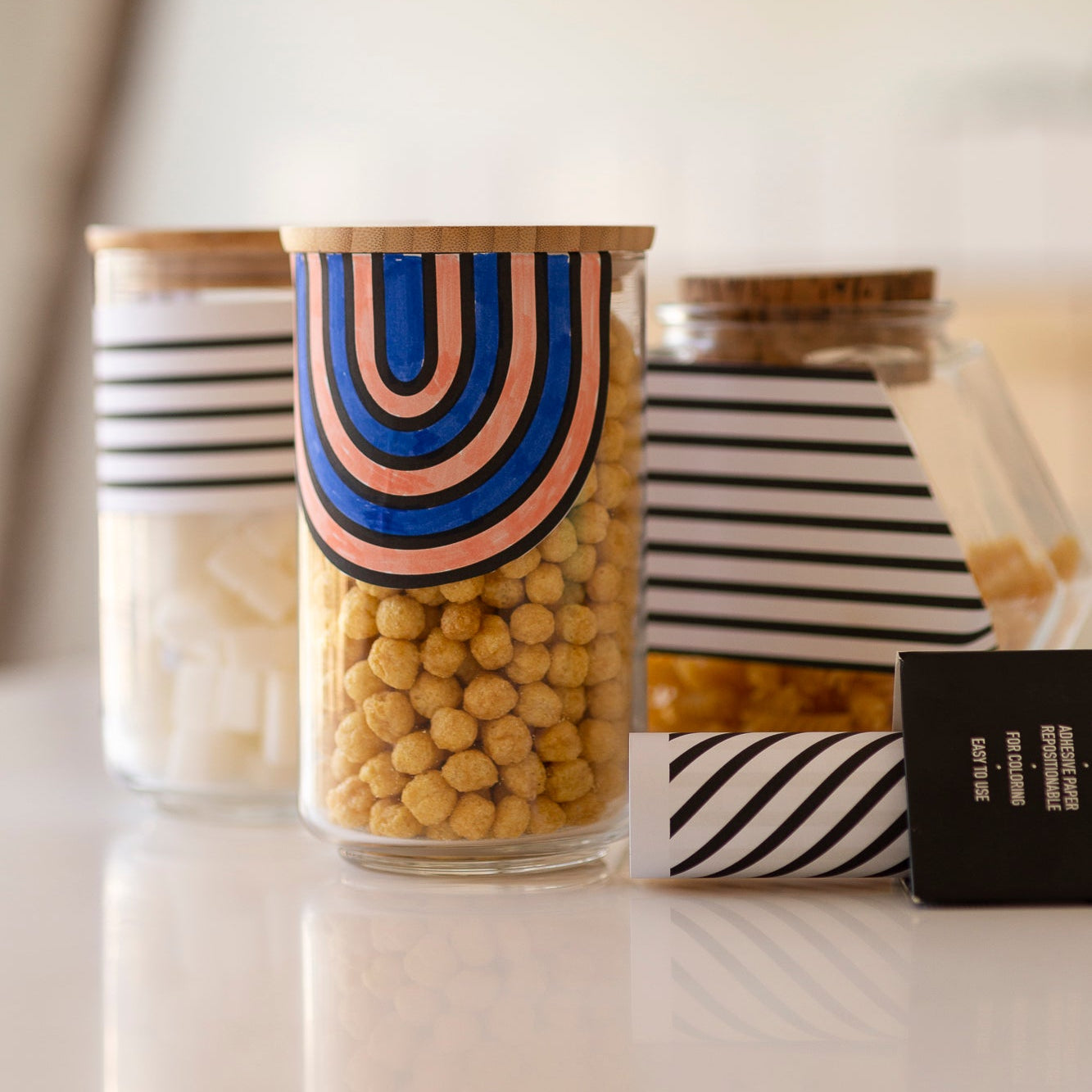 Papier adhésif OMY Stick-it GRAPHIC décorant des bocaux de cuisine avec motifs noir, blanc et arc-en-ciel.