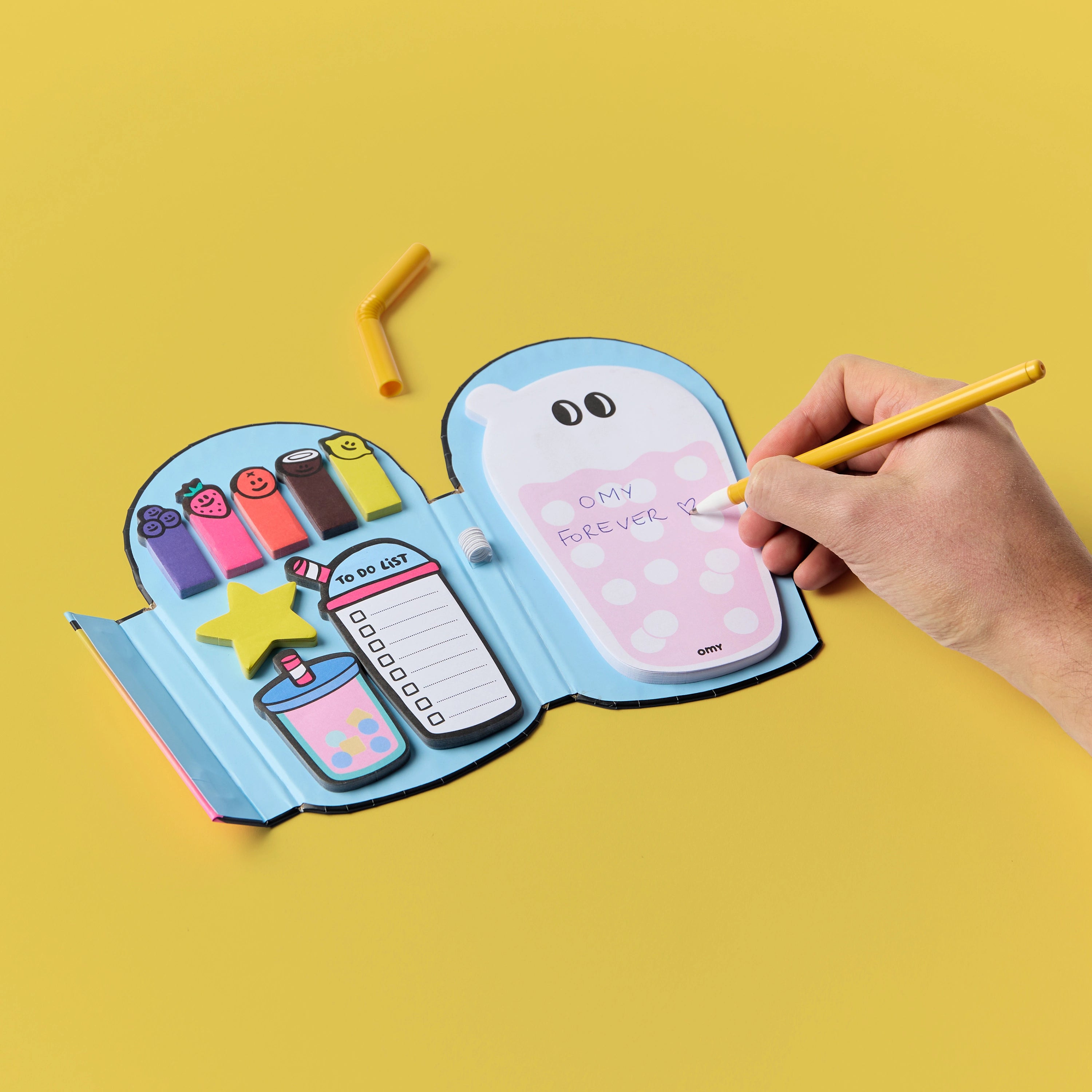 Sticky Notes Bubble OMY ouvert – Mémos repositionnables colorés, to-do list et étoile décorative, une main écrit sur la page, fond jaune