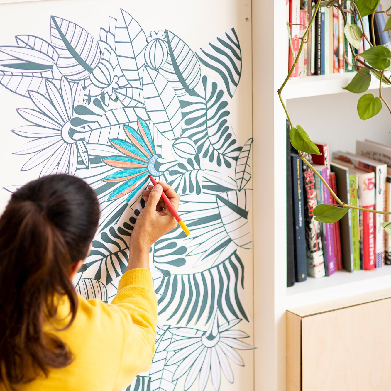Mise en ambiance du rouleau tropical OMY collé sur un mur blanc, entre bibliothèque et plante verte