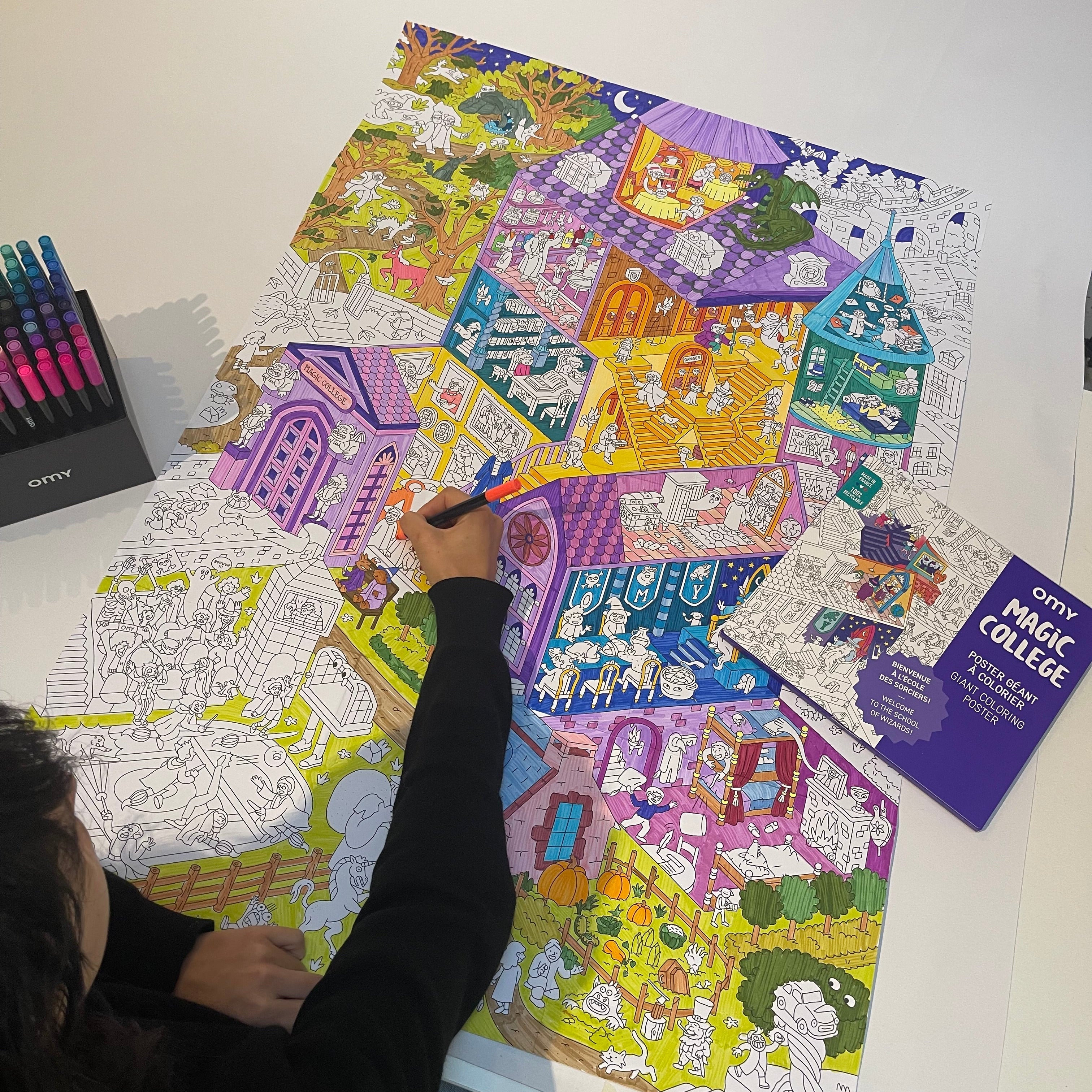 Enfant en train de colorier le poster géant Magic College d’OMY, représentant une école magique pleine de détails colorés – activité ludique et créative à partager.