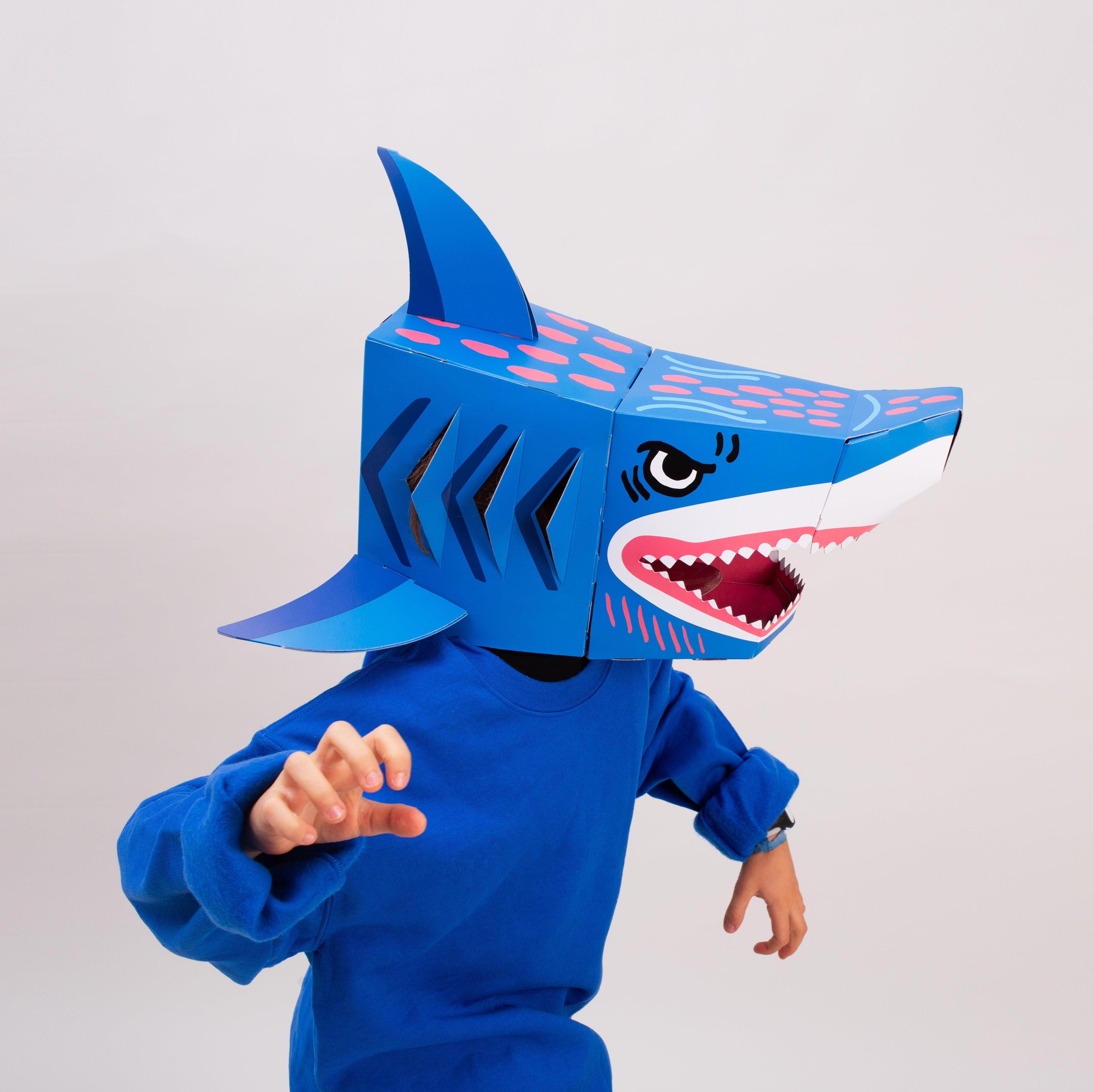 Kind trägt die OMY Sharky 3D-Haimaske aus blauem Karton, Gesicht durch das Maul sichtbar, auf weißem Hintergrund