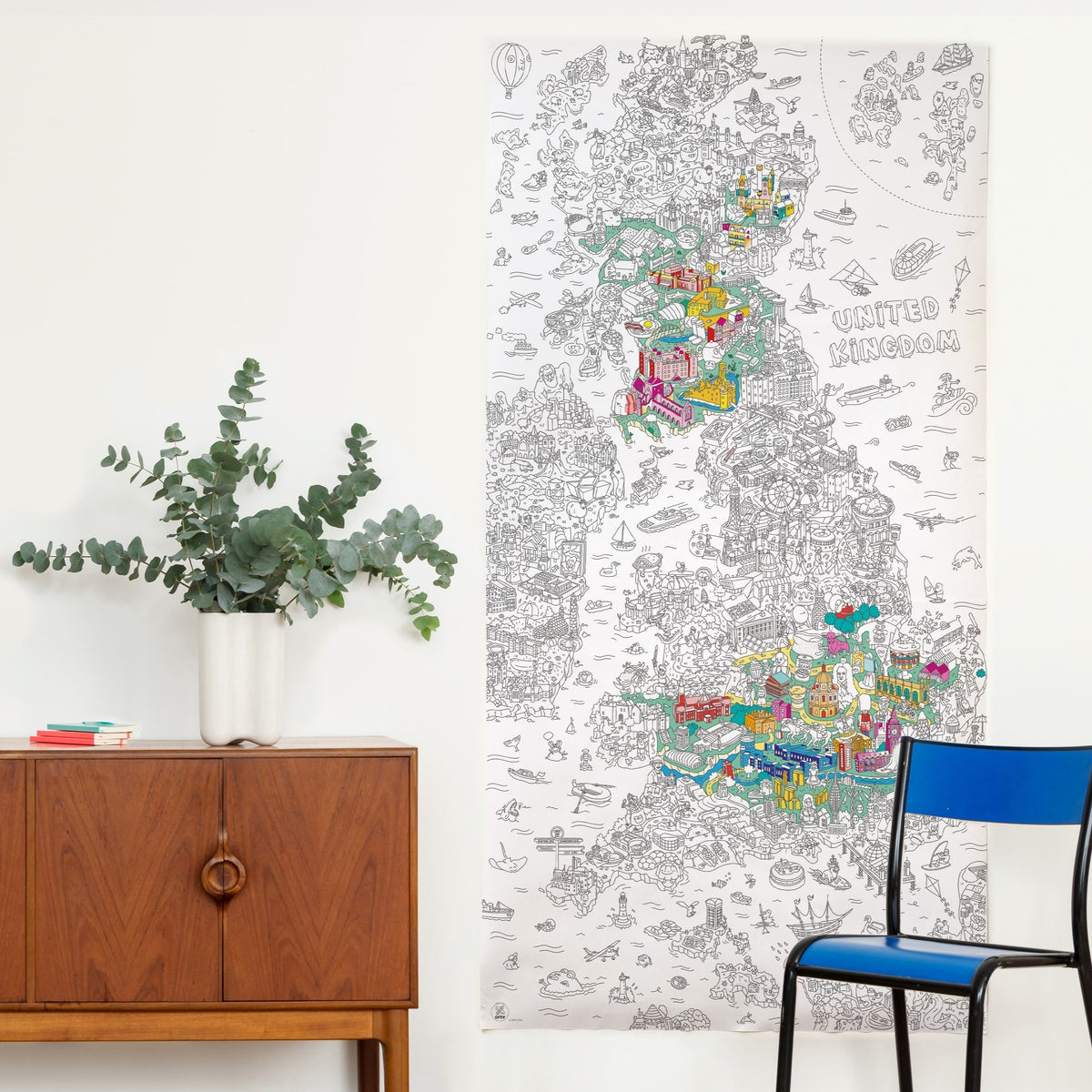 Coloriage géant XXL UK OMY affiché au mur dans un salon, carte du Royaume-Uni en partie coloriée, à côté d'un buffet et d'une chaise bleue