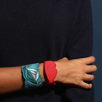 Twee OMY geborduurde armbanden om de pols: blauwgroen bladerwerk en rode lippen, op een marineblauwe trui