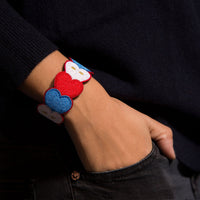 Bracelet brodé OMY à cœurs bleus, blancs et rouges porté au poignet, main dans la poche d'un jean noir