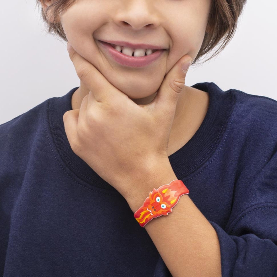 Enfant souriant portant au poignet un bracelet OMY dragon rouge et orange, pull bleu marine