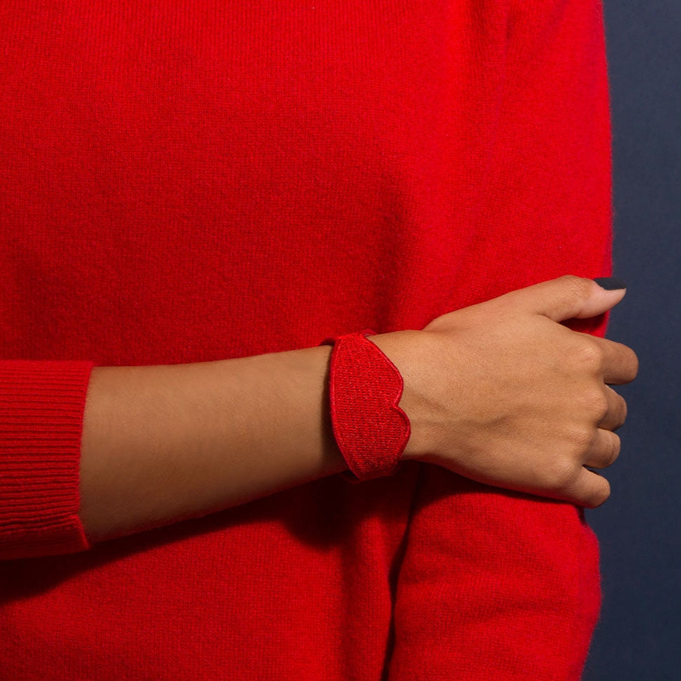 OMY geborduurde armband in de vorm van rode lippen, om de pols gedragen, op een rode trui