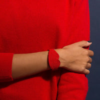 OMY besticktes Armband in Form roter Lippen, am Handgelenk getragen, über einem roten Pullover