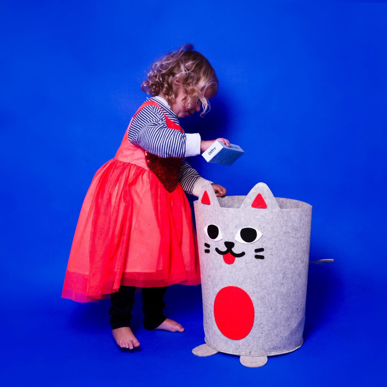 Bazar Bag OMY, panier de rangement en feutrine grise en forme de chat, dans lequel une petite fille range une boîte OMY