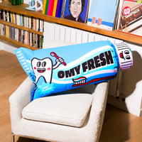 Pufe insuflável OMY Fresh em forma de tubo de dentífrico azul de sabor a menta, pousado numa poltrona branca numa sala.