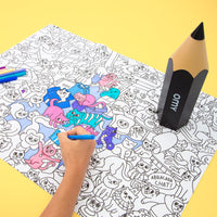 Hand malt mit Filzstift ein Riesenposter OMY mit Katzen aus, neben der schwarzen Riesenstift-Box OMY, auf gelbem Hintergrund.