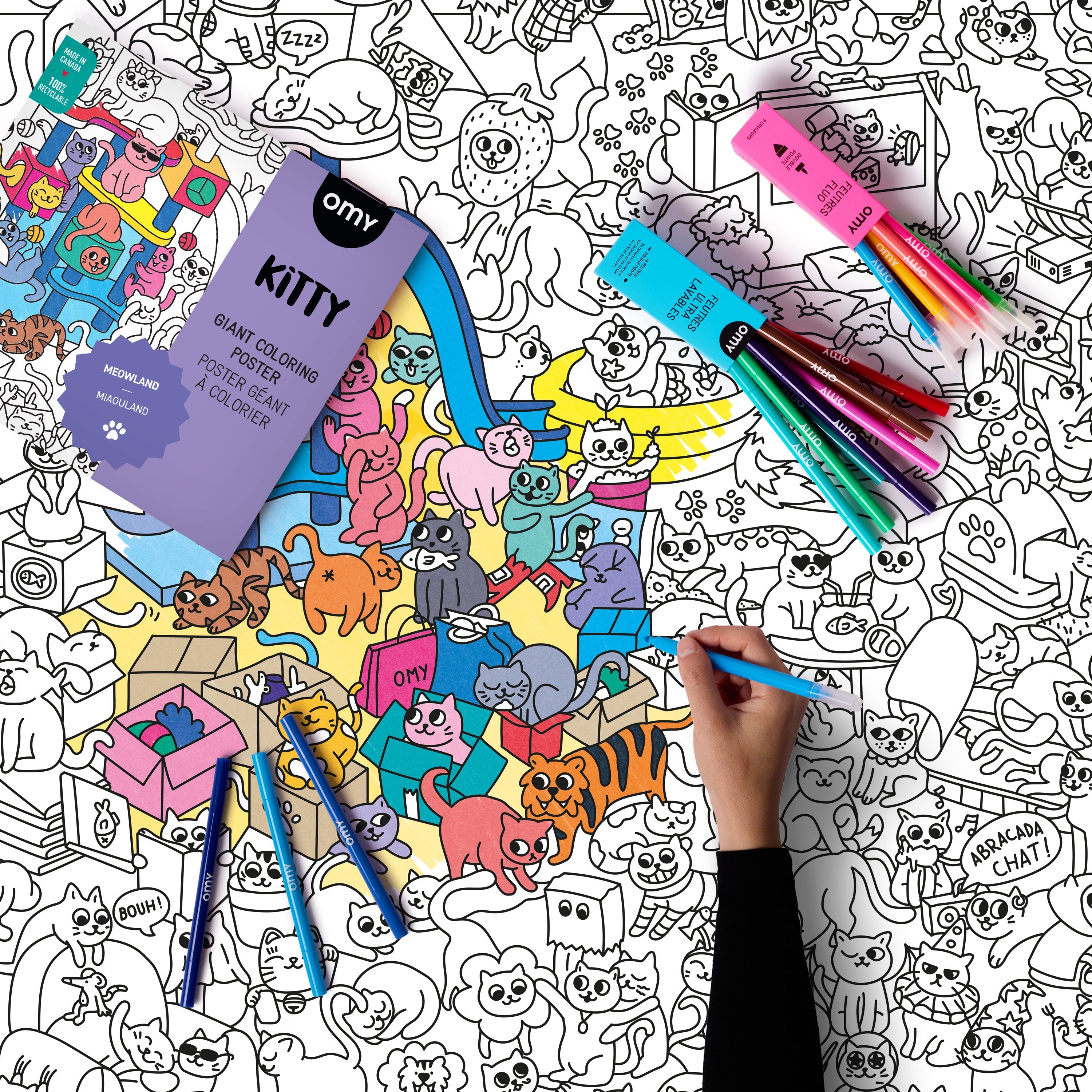 Kind malt die OMY Kitty Box mit Buntstiften und Filzstiften auf einer großen Illustration mit Katzenmotiven aus.
