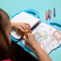 Little girl coloring a basketball-playing dinosaur with a wax crayon in the Dino OMY coloring book, on a turquoise background