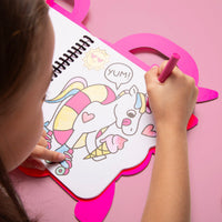 Niña coloreando un unicornio con patines y un helado en el cuaderno para colorear Lily OMY, sobre fondo rosa