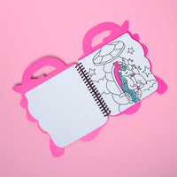 Cuaderno para colorear Lily OMY abierto por una página con un unicornio de melena brillante en un carrusel, sobre fondo rosa
