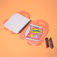 Truck OMY coloring book open to a colored page of a Crispies chip bag, with its 5 wax crayons, on an orange background