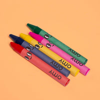 The 5 OMY smiley-face wax crayons included with the Truck coloring book: red, blue, yellow, pink and green, on an orange background