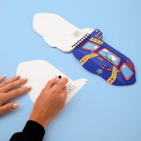 Carnet d'activités stickers Wroum OMY ouvert sur un décor d'avion, avec une main écrivant sur une carte postale détachable