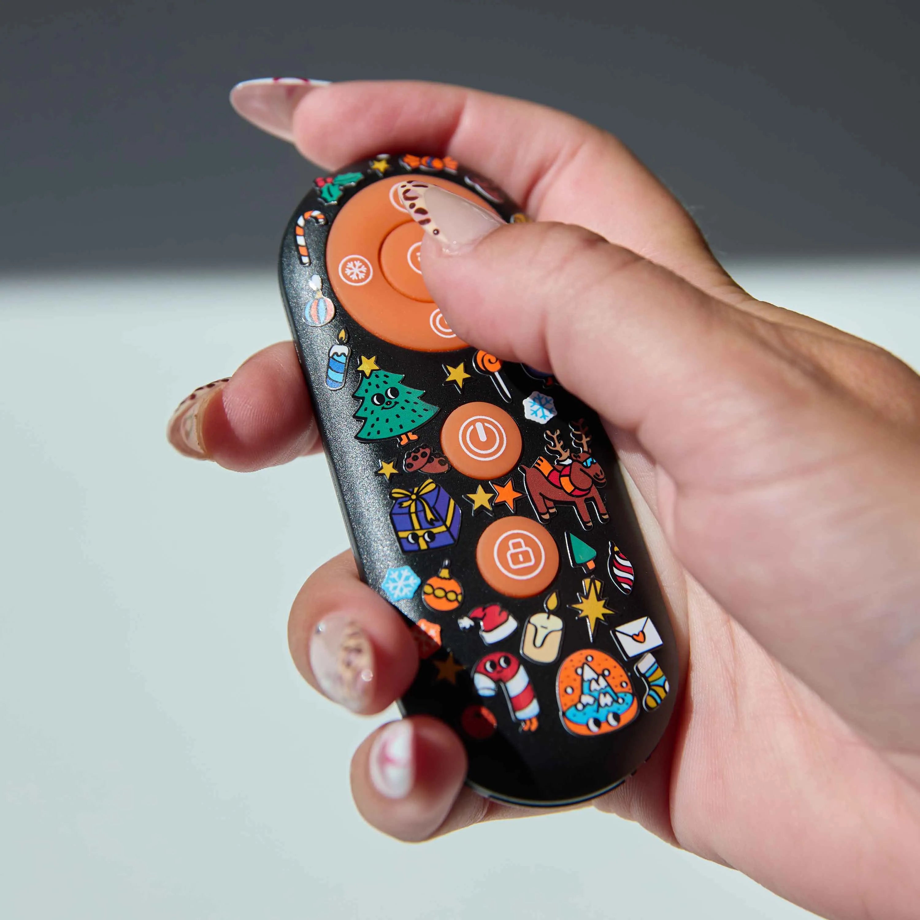 Close-up of a remote control customized with Christmas Boutique Stickers OMY: fir tree, gifts, reindeer and festive decorations.