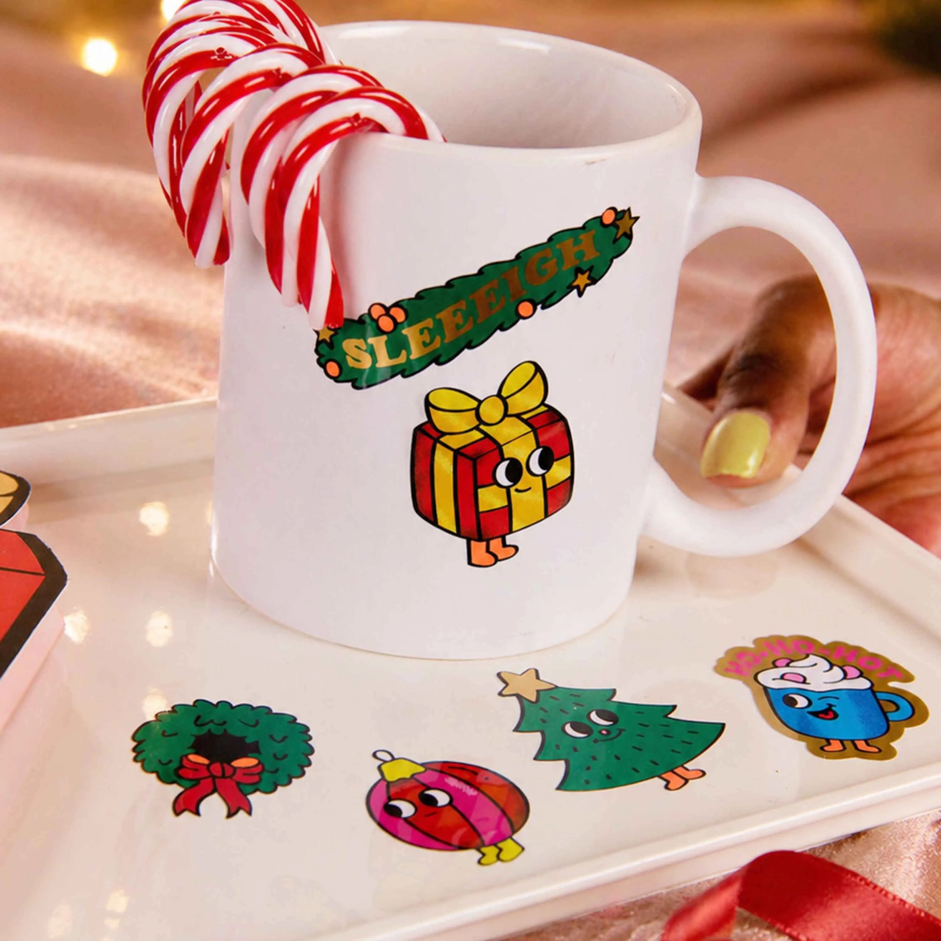 Taza blanca decorada con los Fabulous Stickers Noël OMY, rodeada de stickers festivos y bastones de caramelo.