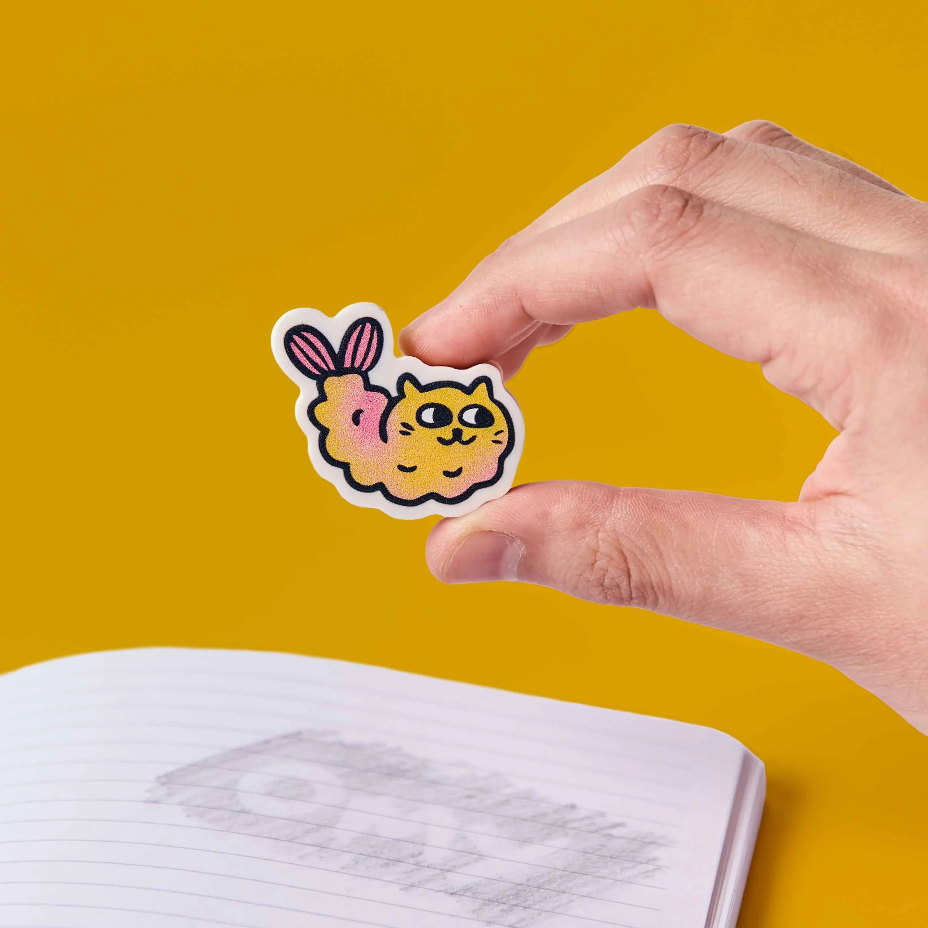 Kawaii-Radiergummi Katze Mewchi OMY in der Hand über einem Schulheft