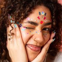 Femme aux cheveux bouclés qui fait un clin d'œil, le visage orné des Face Stickers Flower OMY sur le front et les joues