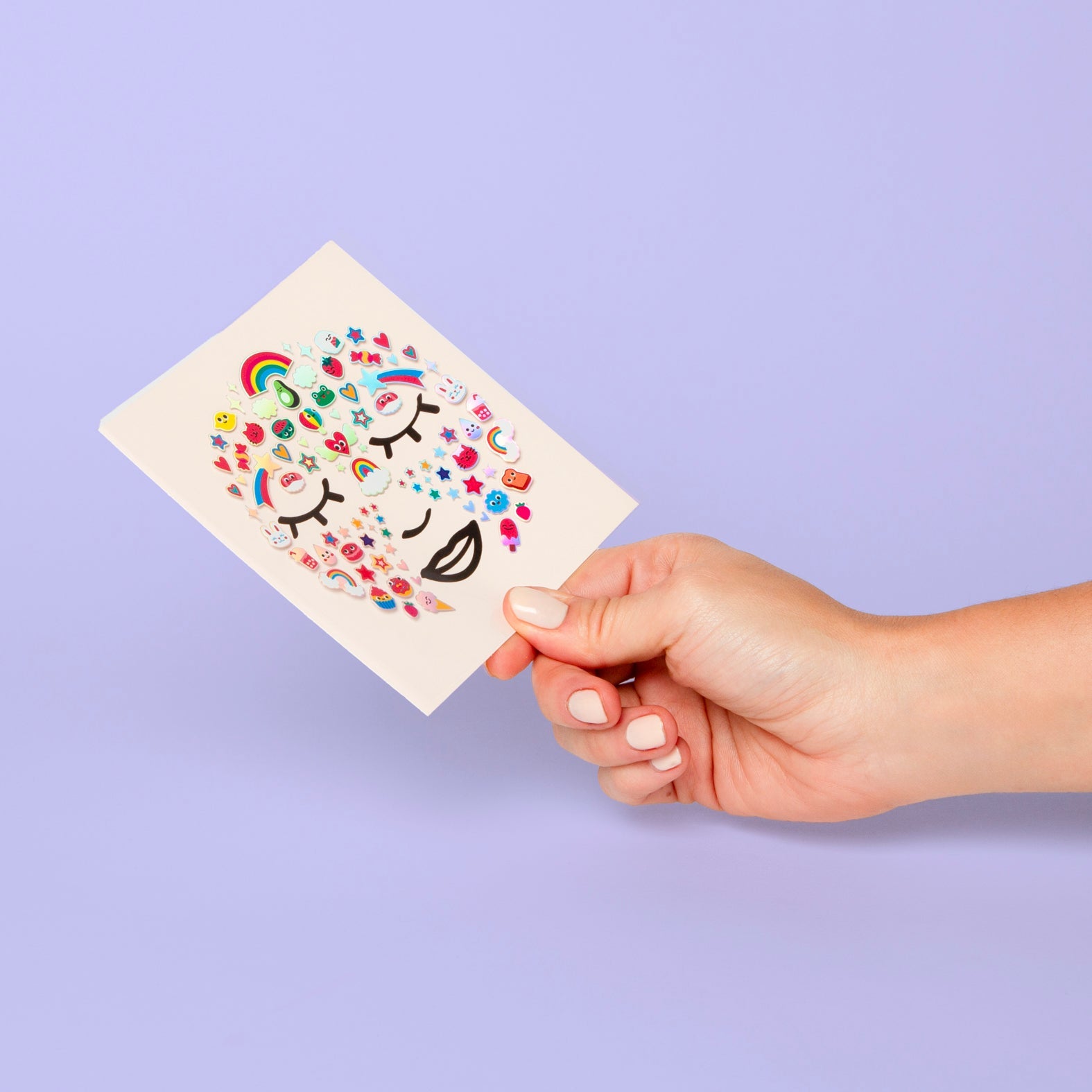 Planche de stickers visage Flower OMY tenue en main : arcs-en-ciel, cœurs et fleurs dessinant un visage, sur fond lilas