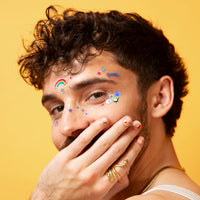 Homme aux cheveux bouclés portant les Face Stickers Kawaii OMY autour de l'œil et sur les ongles, sur fond jaune