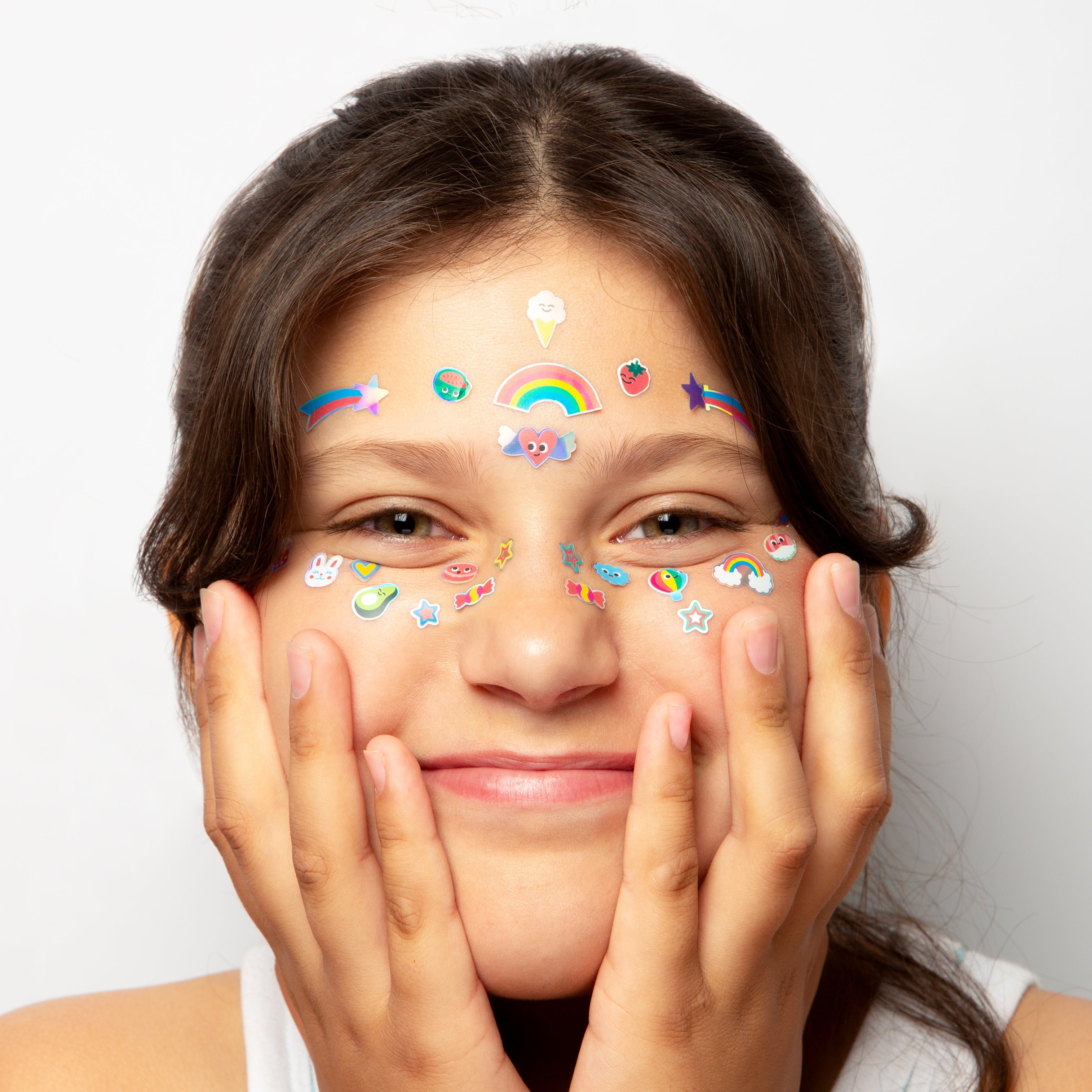 Enfant souriante portant les stickers visage Kawai OMY : arc-en-ciel, étoiles filantes et petits motifs sur le front et les joues