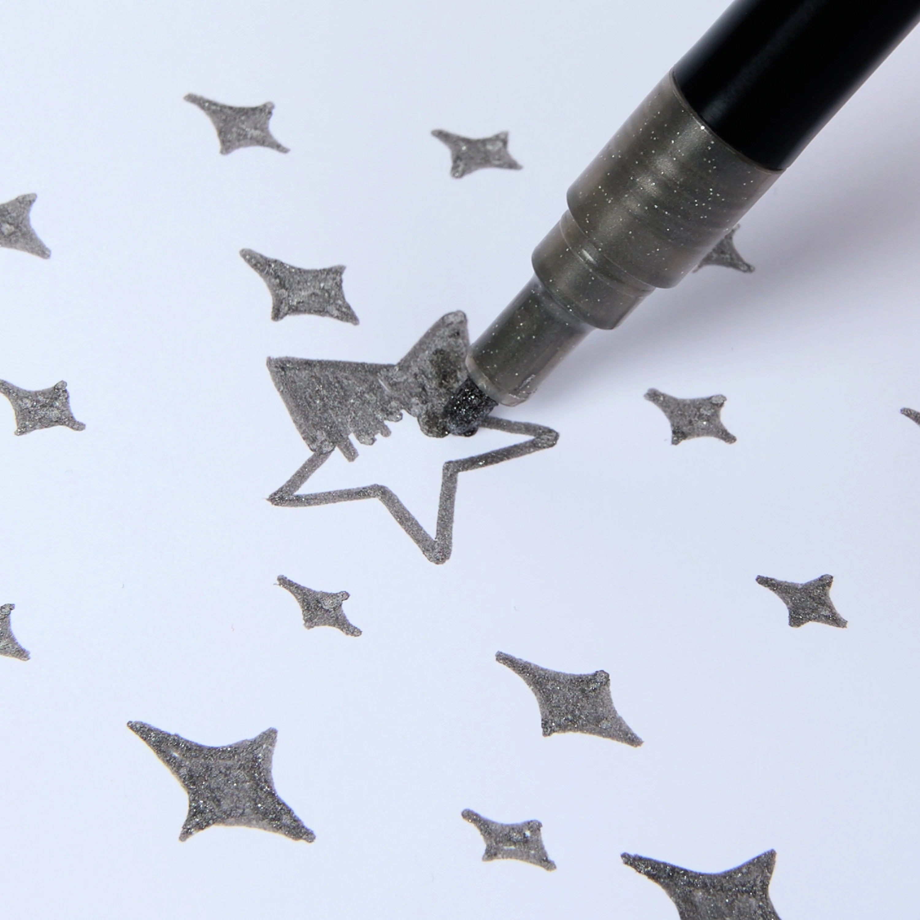 Feutre pailleté argent Glitter Club OMY en train de colorier une étoile sur papier.