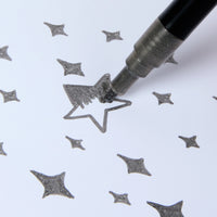 Feutre pailleté argent Glitter Club OMY en train de colorier une étoile sur papier.