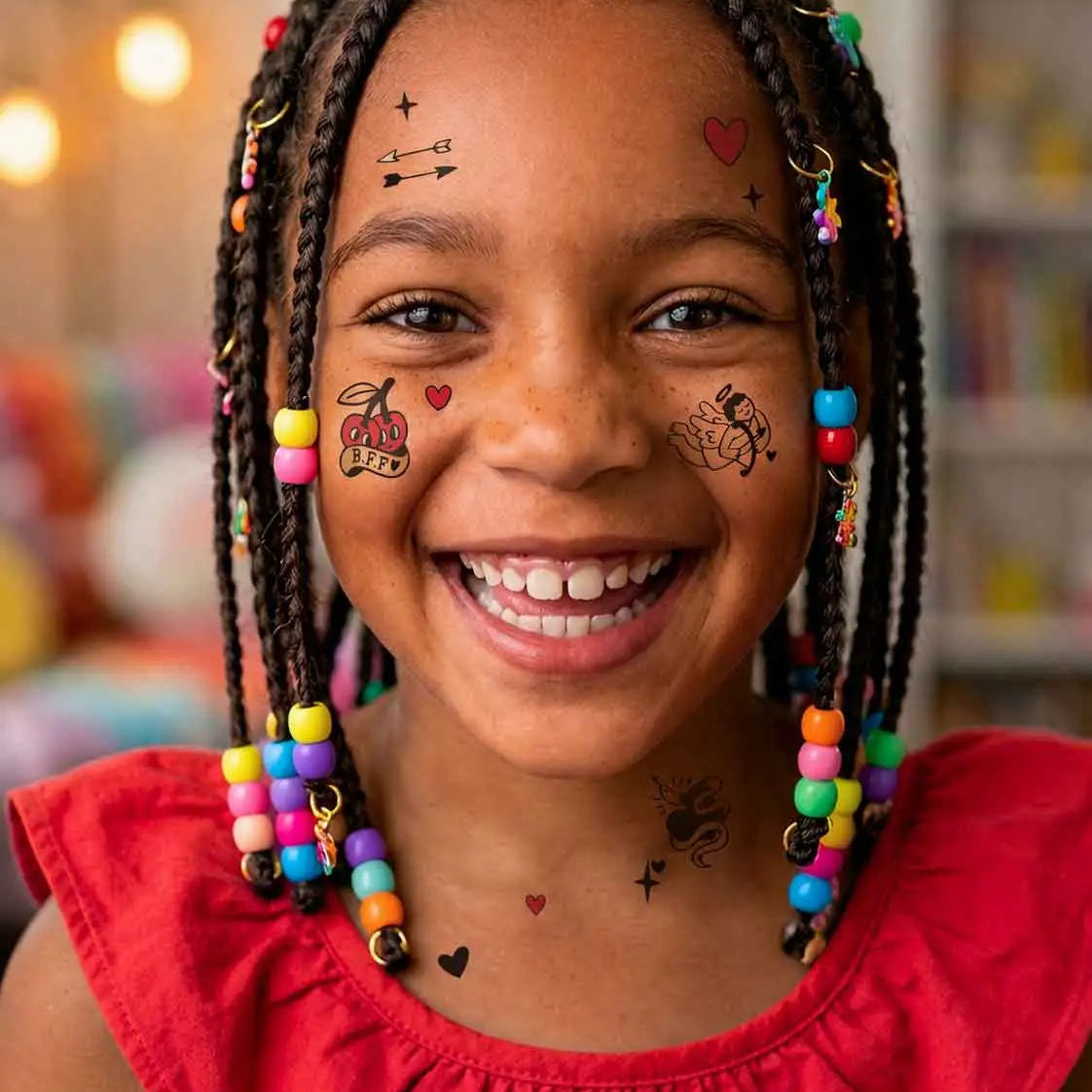 Petite fille souriante avec des tresses colorées portant des tatouages temporaires OMY sur le visage (cœurs, flèches, cerises), collection Flash Tattoos Crazy in Love – modèle Penny