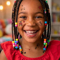 Petite fille souriante avec des tresses colorées portant des tatouages temporaires OMY sur le visage (cœurs, flèches, cerises), collection Flash Tattoos Crazy in Love – modèle Penny