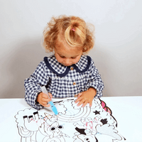 Petite fille coloriant à l'eau un set de table Magic Water OMY avec le stylo à eau, les couleurs de l'arc-en-ciel apparaissent