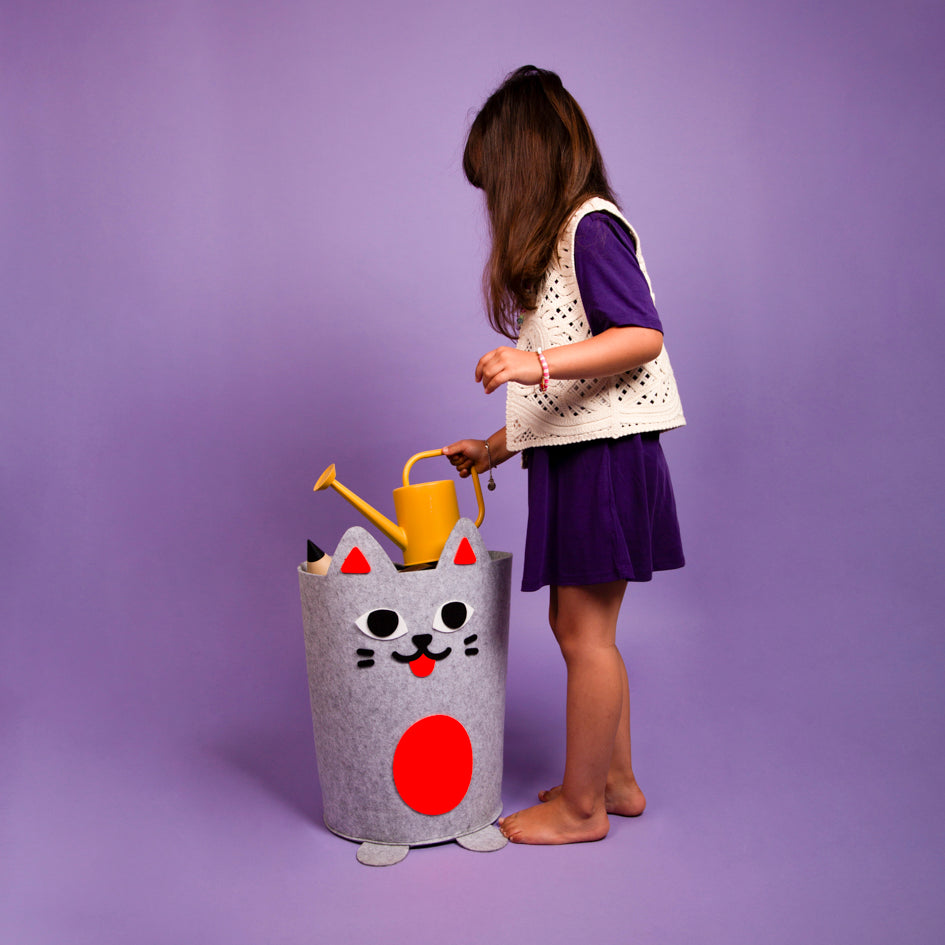 Enfant rangeant un arrosoir dans le Tidy bag Kitty OMY, panier de rangement en feutrine grise en forme de chat, fond violet